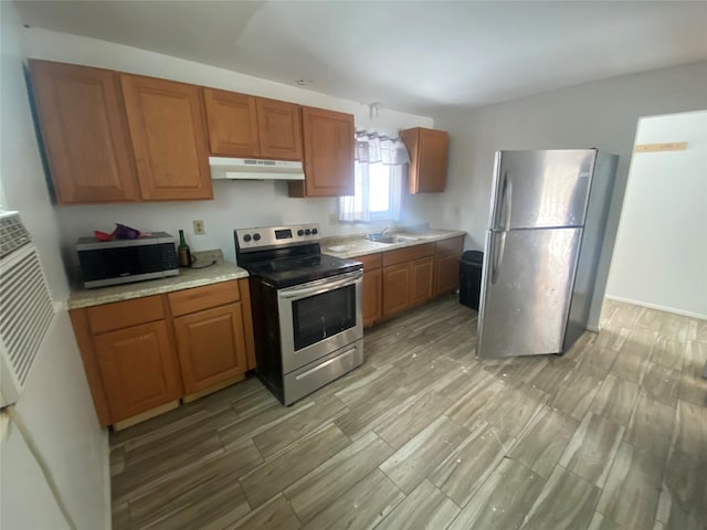 kitchen featuring brown cabinetry, stainless steel appliances, light countertops, under cabinet range hood, and a sink