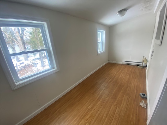 spare room featuring a baseboard heating unit, baseboards, and wood finished floors