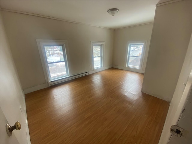 empty room featuring a baseboard heating unit, crown molding, and light wood finished floors