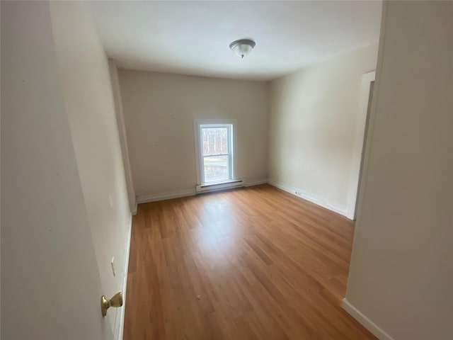 spare room featuring a baseboard heating unit, light wood-type flooring, and baseboards