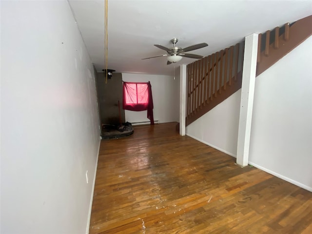 interior space with stairway, a baseboard heating unit, ceiling fan, wood finished floors, and baseboards