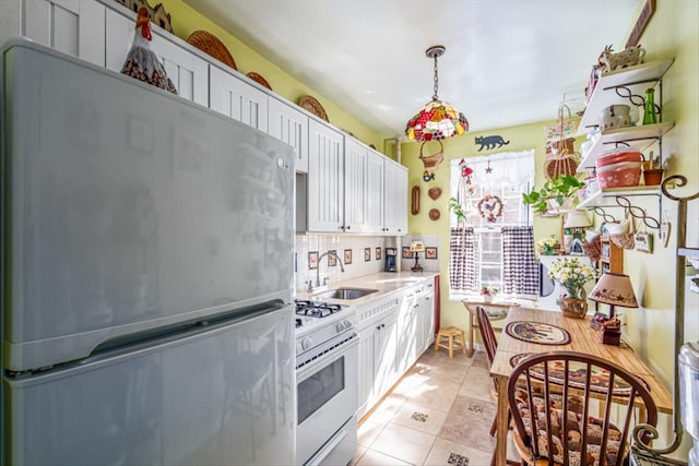 kitchen with white gas stove, a sink, white cabinets, light countertops, and freestanding refrigerator