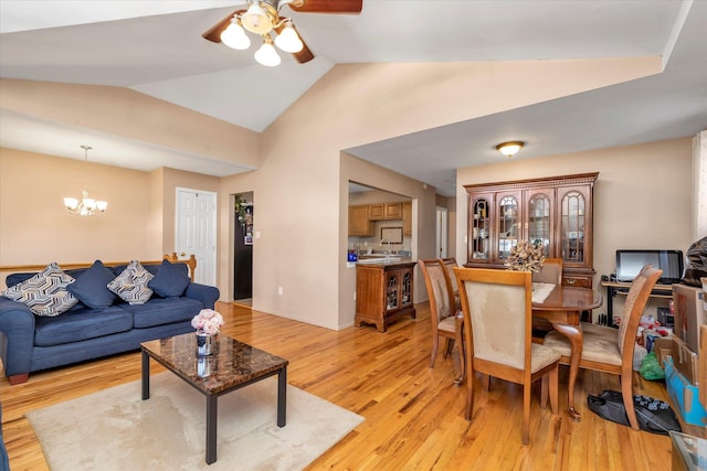 dining space featuring light wood finished floors, ceiling fan with notable chandelier, baseboards, and vaulted ceiling