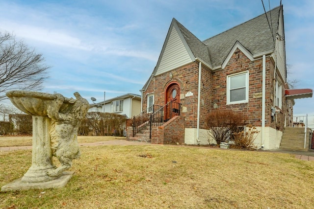 tudor home featuring brick siding, roof with shingles, and a front yard