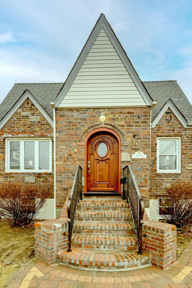 property entrance featuring roof with shingles and brick siding