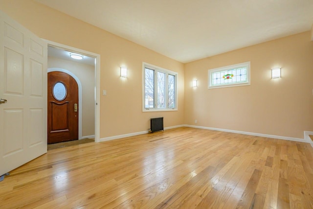 foyer featuring arched walkways, radiator heating unit, light wood-style flooring, and baseboards