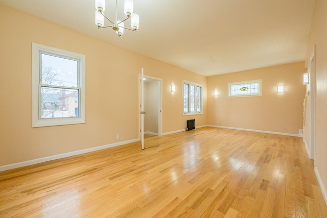 unfurnished room with light wood-type flooring, an inviting chandelier, and baseboards