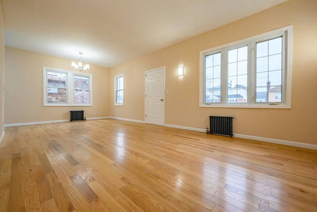 unfurnished living room featuring a notable chandelier, radiator heating unit, baseboards, and light wood-style floors