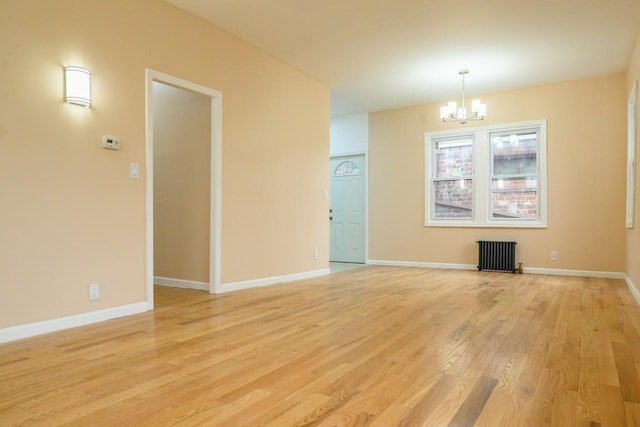 spare room featuring a chandelier, baseboards, light wood-style flooring, and radiator