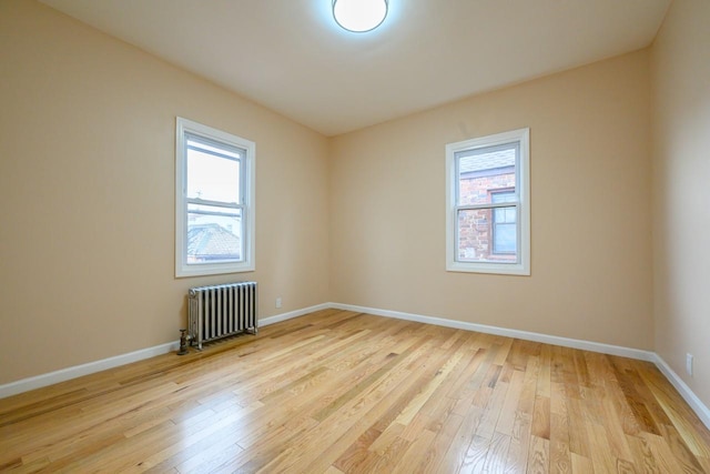 empty room with radiator, light wood-style floors, and baseboards