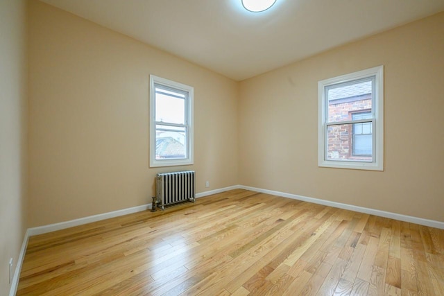 spare room with light wood-type flooring, baseboards, and radiator heating unit