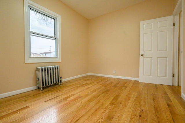 empty room featuring radiator, baseboards, and light wood finished floors