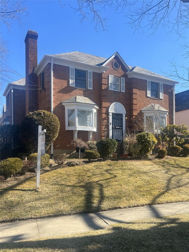 traditional home featuring a front yard, a chimney, and brick siding