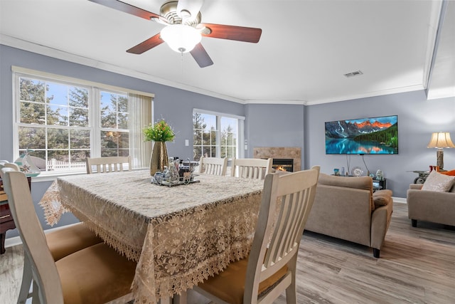 dining space featuring visible vents, light wood-style flooring, ornamental molding, a warm lit fireplace, and baseboards