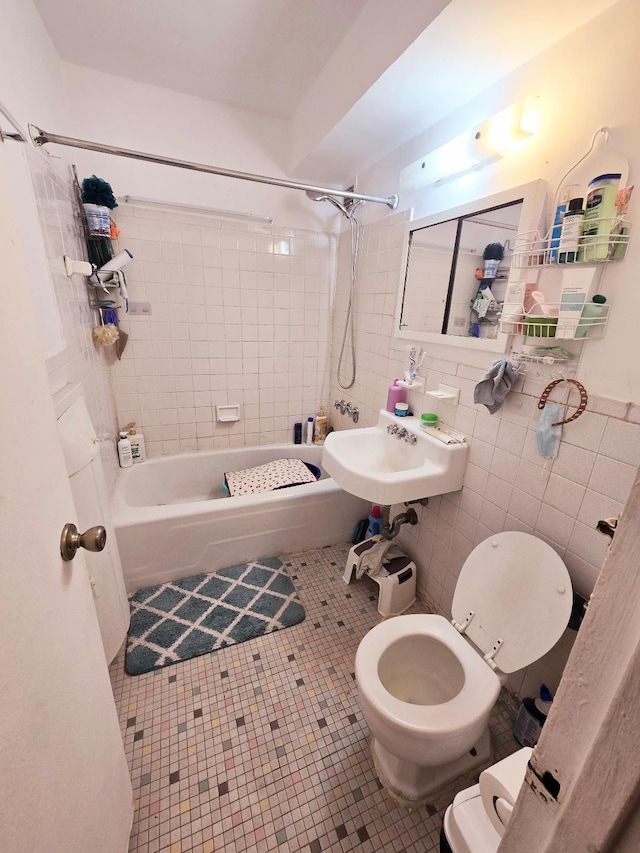 full bathroom with tile walls, toilet, tile patterned floors, washtub / shower combination, and a sink