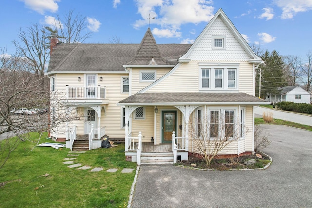 victorian house with a front yard, covered porch, and roof with shingles