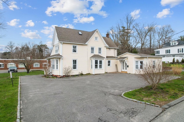 view of front of house with roof with shingles, aphalt driveway, and a chimney