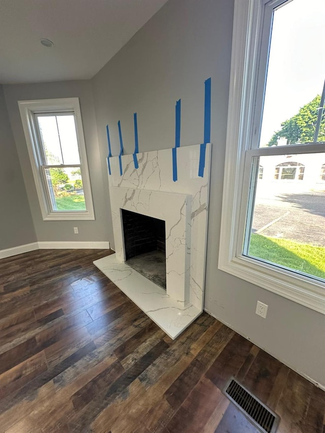 unfurnished living room featuring dark wood-style flooring, visible vents, baseboards, and a premium fireplace