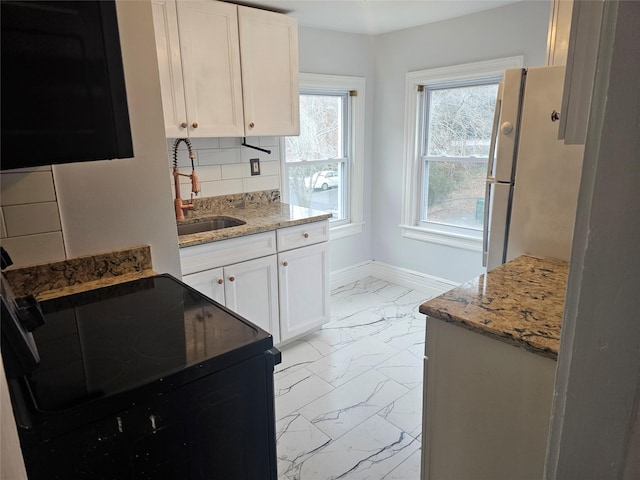 kitchen featuring decorative backsplash, freestanding refrigerator, marble finish floor, black / electric stove, and a sink