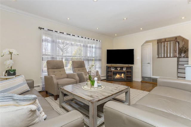 living room featuring a glass covered fireplace, ornamental molding, wood finished floors, stairs, and a baseboard heating unit