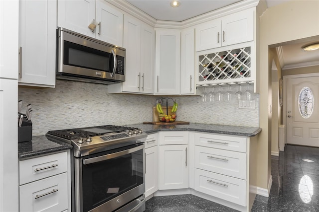 kitchen featuring appliances with stainless steel finishes, ornamental molding, dark stone countertops, granite finish floor, and white cabinetry