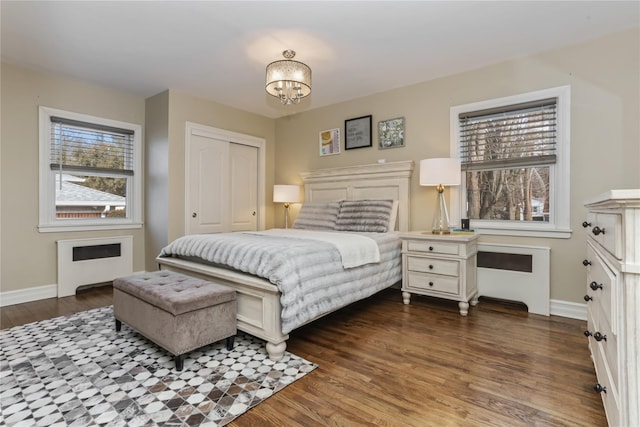 bedroom featuring a chandelier, baseboards, a closet, dark wood-style floors, and radiator heating unit