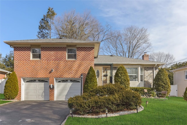 tri-level home with aphalt driveway, brick siding, a chimney, a garage, and a front lawn