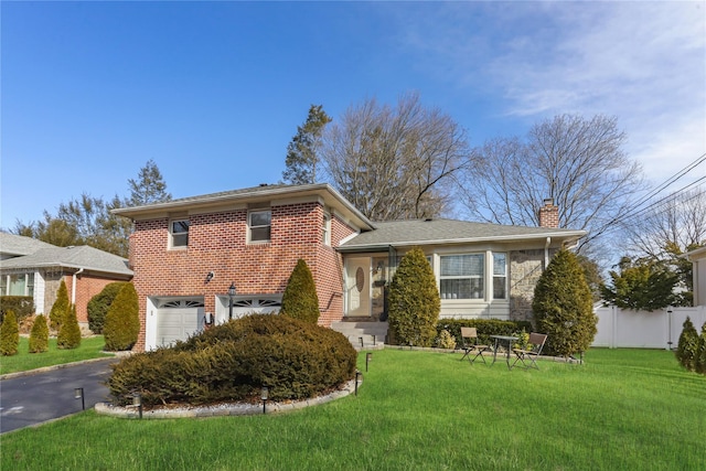 split level home with driveway, fence, a front lawn, and brick siding