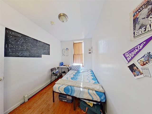 bedroom with a baseboard heating unit, wood finished floors, and baseboards