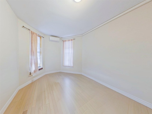 empty room with light wood-style floors, baseboards, and a wall mounted air conditioner