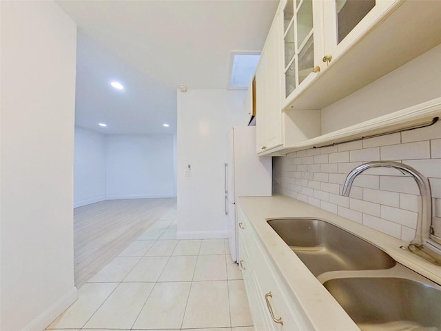 kitchen featuring a sink, white cabinetry, light countertops, decorative backsplash, and glass insert cabinets