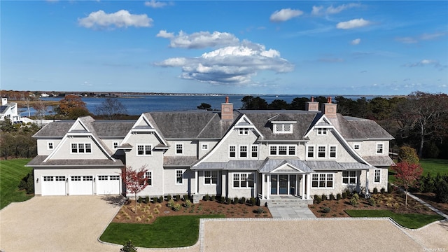 shingle-style home with a garage, a water view, a chimney, and driveway