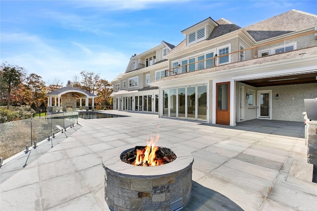 rear view of property with a gazebo, a balcony, a fire pit, and a patio