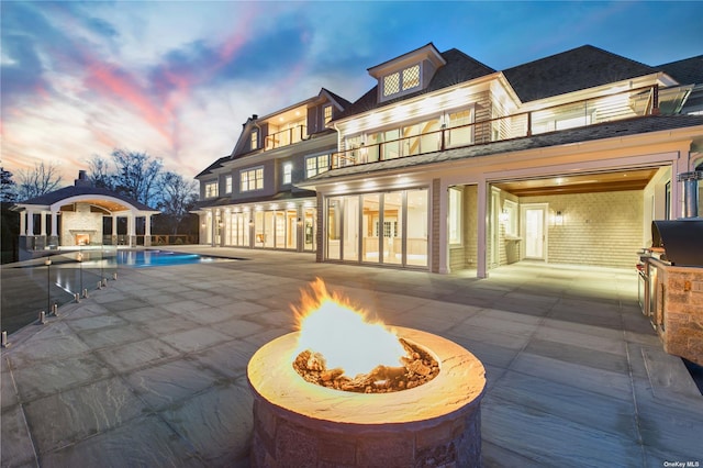 back of house at dusk with an outdoor pool, a patio area, a balcony, and an outdoor fire pit