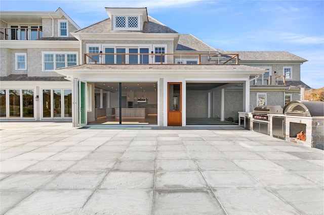 rear view of property with a balcony, a patio area, and an outdoor kitchen