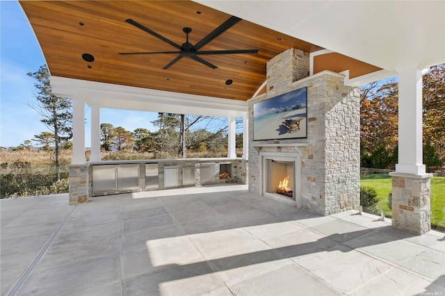 view of patio featuring a gazebo, exterior kitchen, an outdoor stone fireplace, and a ceiling fan