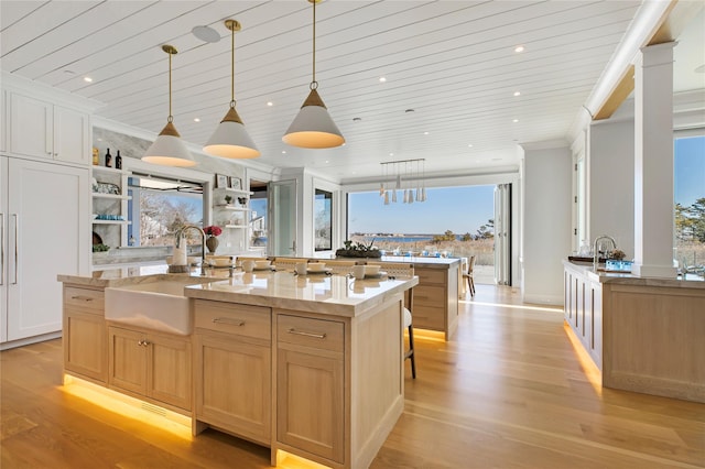 kitchen with a sink, open shelves, a kitchen island with sink, and light wood-style flooring