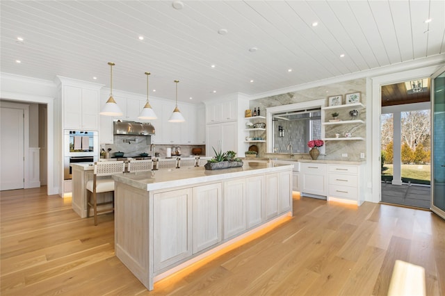 kitchen featuring backsplash, under cabinet range hood, ornamental molding, a large island, and open shelves