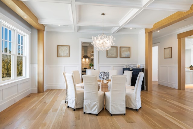 dining room with an inviting chandelier, beam ceiling, light wood-style flooring, and a decorative wall