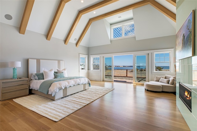 bedroom with beamed ceiling, high vaulted ceiling, access to outside, wood finished floors, and a lit fireplace