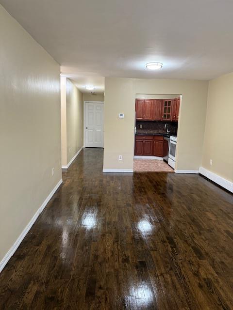 unfurnished living room featuring dark wood finished floors and baseboards