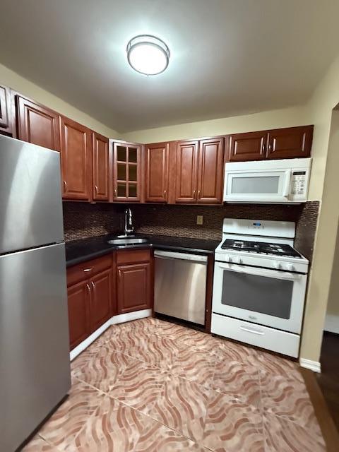 kitchen with dark countertops, decorative backsplash, appliances with stainless steel finishes, glass insert cabinets, and a sink