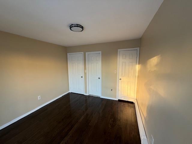 unfurnished bedroom with two closets, dark wood finished floors, and baseboards