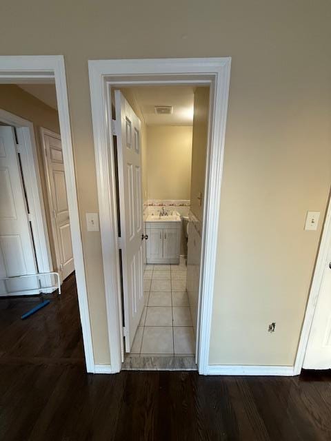 corridor featuring visible vents, a sink, baseboards, and wood finished floors