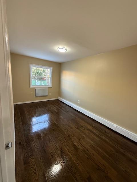 spare room featuring a wall unit AC, dark wood-style floors, and baseboards