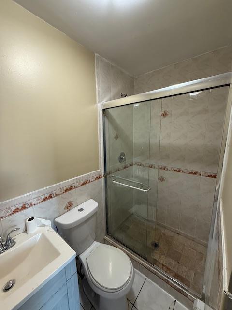 bathroom with toilet, a stall shower, tile walls, and vanity