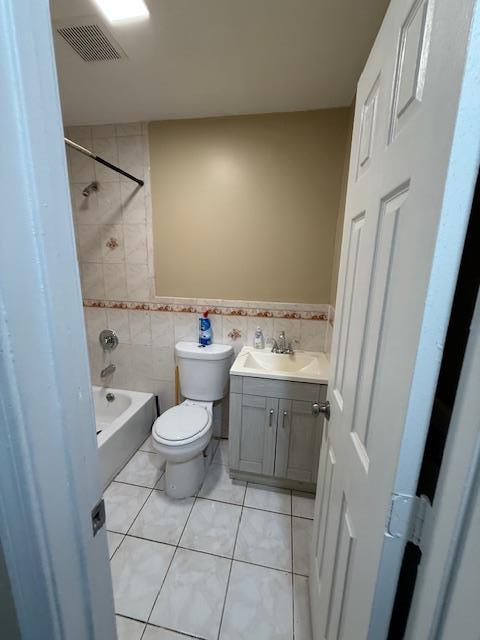 full bath featuring tile walls, visible vents, toilet, vanity, and tile patterned floors