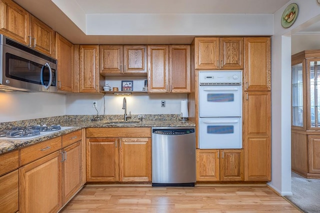 kitchen featuring brown cabinets, a sink, dark stone countertops, appliances with stainless steel finishes, and light wood finished floors