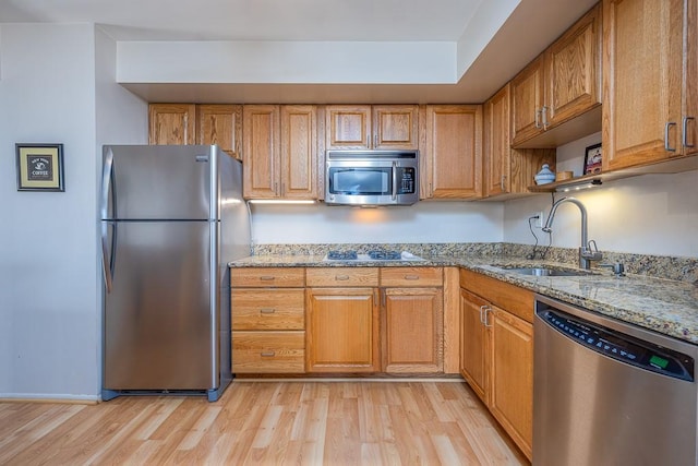 kitchen featuring light stone counters, brown cabinetry, a sink, appliances with stainless steel finishes, and light wood-type flooring