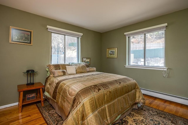 bedroom featuring baseboard heating, multiple windows, and wood finished floors